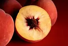 Photograph showing a peach in cross section with yellow flesh and a single large reddish brown pit