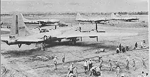 Four large 4-engined World War II-era aircraft sitting on the ground at an airstrip. Groups of people are working near each aircraft.