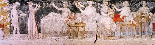 A banquet scene from a Macedonian tomb of Agios Athanasios, Thessaloniki, 4th century BC; six men are shown reclining on couches, with food arranged on nearby tables, a male servant in attendance, and female musicians providing entertainment.