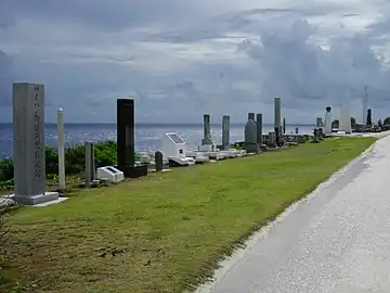 various cenotaphs on grass lined up from lower left to mid right side with ocean in background.