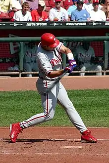 A man in a Philadelphia Phillies' uniform swinging a baseball bat