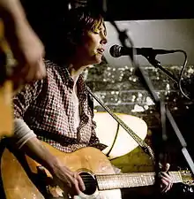 A woman playing guitar and singing into a microphone stand