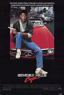 Axel Foley (portrayed by Eddie Murphy) sits on the hood of a red Mercedes-Benz convertible with a pistol pointing out on his left hand and his left foot resting above the word "Hills". The caption above reads "He's been chased, thrown through a window, and arrested. Eddie Murphy is a Detroit cop on vacation in Beverly Hills."