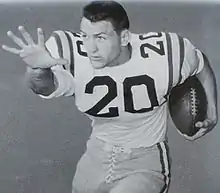 Black and white posed shot of Cannon from the thighs up, in the stiff-arm position, cradling a football, wearing pads and a jersey number 20, helmetless