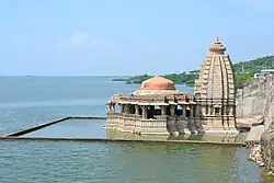 A Hindu temple with water submerged courtyard near a dam's reservoir.