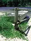 A metal rowboat chained to a metal pole with a lake behind