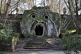 A moss-covered sculpture of an ogre's head in a garden.