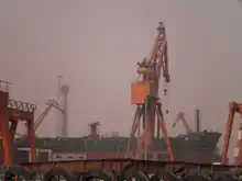 An unfinished ship and an orange crane at the center of an industrial setting