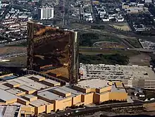 A tall, reflective, bronze-colored hotel tower sits atop a smaller structure, next to a parking garage.  A highway and city streets are visible in the background.