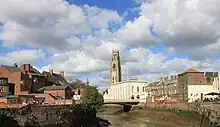 A small river, with houses on either side and a church spire in the background