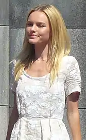 Young blond woman, straight hair below shoulders, wearing a plainly styled, white embossed dress