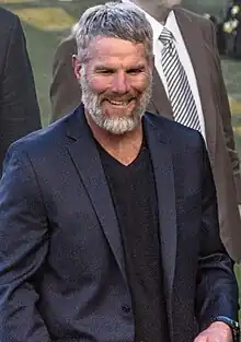 Favre smiling, wearing a suit, standing on a football field