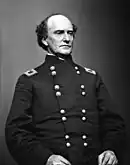 Black and white photo of a clean-shaven, balding man. He wears a dark military uniform with two rows of buttons.