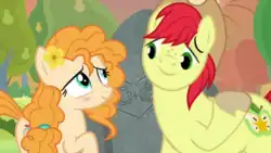 A female orange pony and a male yellow pony stand in front of a carved rock, looking at each other lovingly.