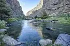 A stream calmly flows by at the bottom of light gray cliffs