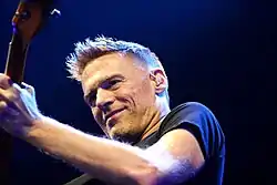  A close up color photo of a man playing the guitar, wearing a black T-shirt .