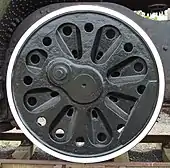 An almost solid disc (not spoked) locomotive wheel with a series of cast-in radial indentations and prominent round holes intended to reduce its weight.