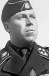 A man wearing a military uniform and side cap. His cap has an emblem in shape of a human skull and crossed bones.