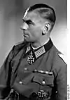 A man wearing a military uniform, facing left of the viewer. Dressed in German World War II Officer uniform with a neck order in the shape of a cross.