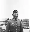 A man wearing a side cap, military uniform with an Iron Cross displayed at the front of his uniform collar.