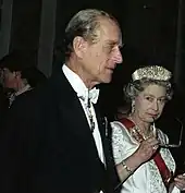 Elizabeth, in formal dress, holds a pair of spectacles to her mouth in a thoughtful pose