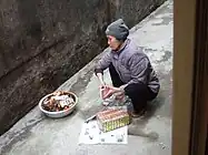 Woman burning joss papers in front of her house in Hanoi after having offered food to her ancestors