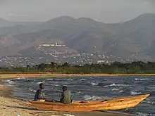 two sitting in skiff on beach on lakeshore with mountains in bckround