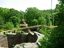 The Loch Ness Monster's second lift hill and mid-course brake run is viewed in the image among green foliage and trees. The mid-course brake run is above the second lift hill in the center image. The tunnel's exterior structure can also be seen in the bottom left.