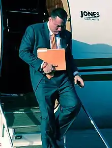 Man in blue suit carrying an orange folder existing a small jet plane