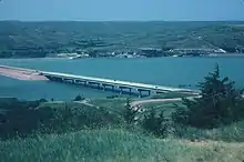 Distant view of a simple highway bridge crossing a wide river surrounded by rolling hills free of vegetation