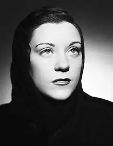 A dark haired woman of about 22 years of age wearing a black, hooded outfit, stares off to the right