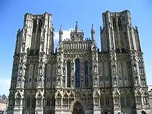 Large ornate grey stone facade of a building. Symmetrical with towers either side.