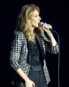 Celine Dion holding a microphone against a black background