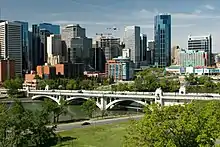 A photograph of a cityscape with tall buildings in the background, a green park in the foreground, and a white bridge in the middle