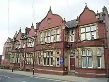 The front of a red-brick two-storey structure that is viewed from the ground upwards. It has a complex facade of four Dutch gables with many windows at regular intervals.