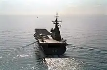 A small aircraft carrier photographed from behind as she sails across calm waters