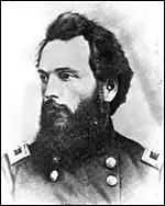 Black and white photo shows a bearded and dark-haired man in a dark uniform with two rows of buttons.