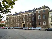 Three story palace with two large wings.  Many decorative elements such as cornices, window pediments, and a stone balcony over the entrance.