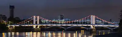 Night view of a lit suspension bridge over a wide river, which reflects the light from the bridge.