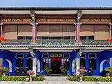 Front façade of a double-storey Oriental-style mansion, coloured in blue and with the upper floor partially concealed by wooden blinds.