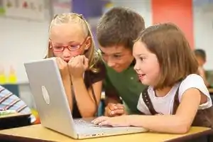 Three young students seated and viewing a laptop in a classroom