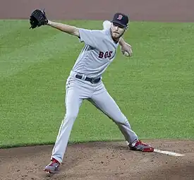 A man in a grey baseball uniform with "Boston" on the front throws a pitch.