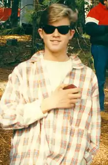 A male in a plaid shirt wearing sunglasses smiling toward a camera