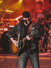 Singer Chris Young, strumming an acoustic guitar wile singing into a microphone.