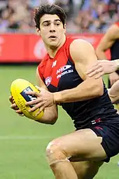 Male athlete in sleeveless guernsey runs  holds football