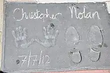 A hand and footprint reading "Christopher Nolan" at the top and "7/7/2012" at the bottom.