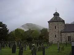 The tower and churchyard, with numerous trees and a large hill behind them.