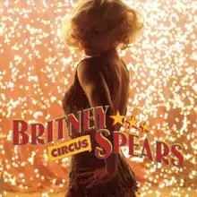 The torso of a Britney Spears with a wavy blond haircut wearing a sparkly golden dress. She is looking over her shoulder, with her left hand resting on her left hip. In the back, there is a shower of sparks. The words "BRITNEY" followed by three yellow stars and "SPEARS" are written in capital red circus-like handwriting. Below "BRITNEY", the word "CIRCUS" is written in smaller capital letters.