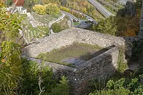 Set of low walls that form a rectangle on the ground. In the centre of the rectangle is a metal trap door.