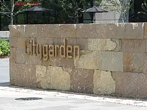 The word "Citygarden" in gold metal letters is fixed to a low wall made of golden-yellow rock bricks.